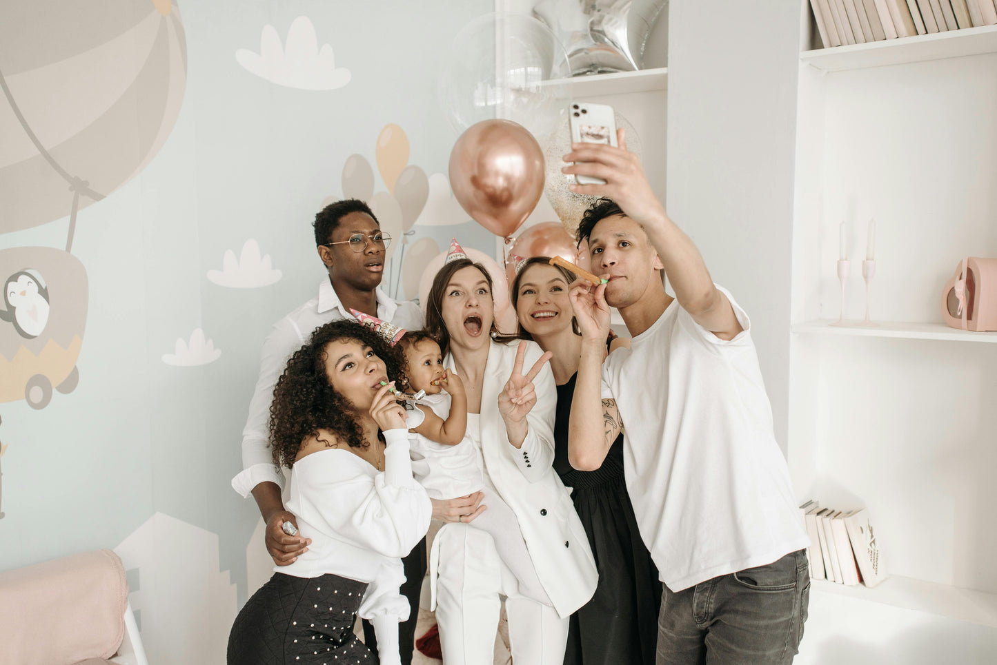 Group of young adults and a young child taking a selfie video with phone in a baby's room.