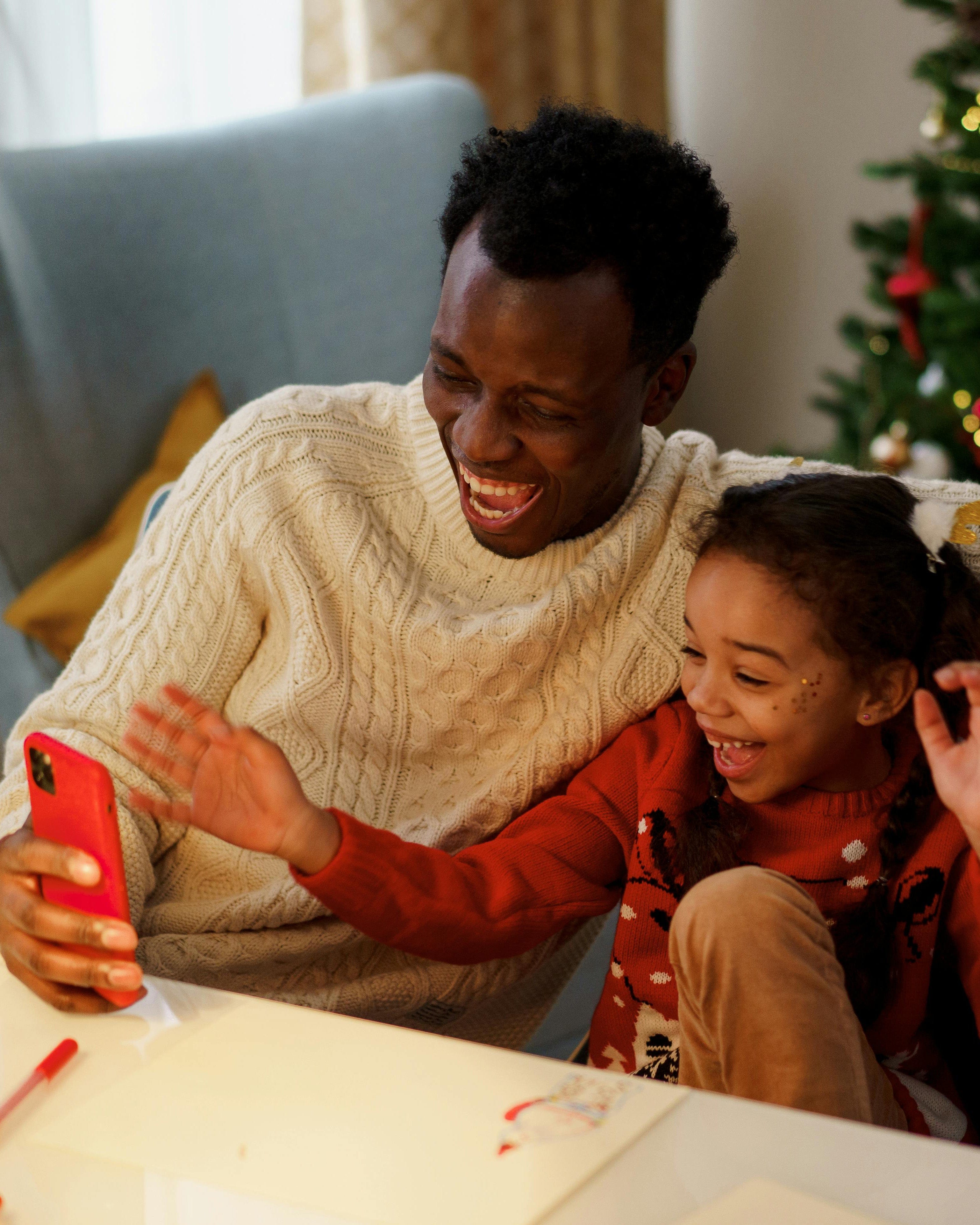 Father and daughter laughing and watching a video on a phone during Christmas time - Holidays video editing service.