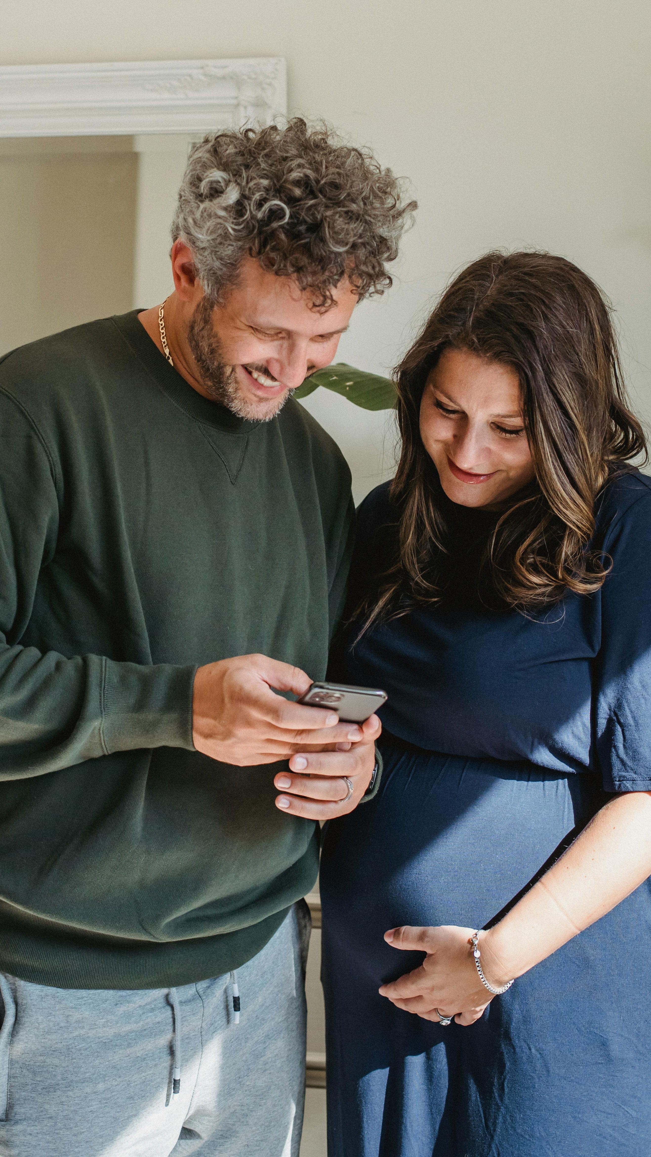 Smiling man and woman pregnant couple watching a video on their phone – pregnancy video editing service.